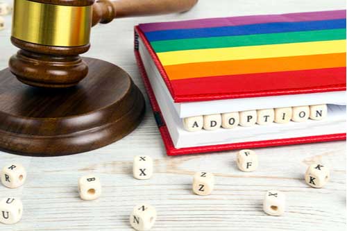 Book with rainbow gay pride flag and blocks spelling adoption, concept of Fayetteville LGBT family law attorney