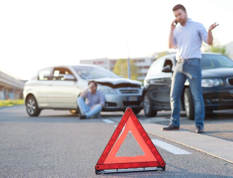 A red warning triangle is on the road with drivers on their phones and damaged vehicles in the background and they are consulting an auto accident lawyer after the crash in Georgia.