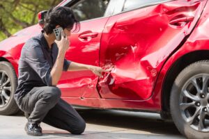 Understanding Liability in Multi-Vehicle Collisions A man looking at the damage on his car while on the phone after being in apart of multi-vehicle collisions.